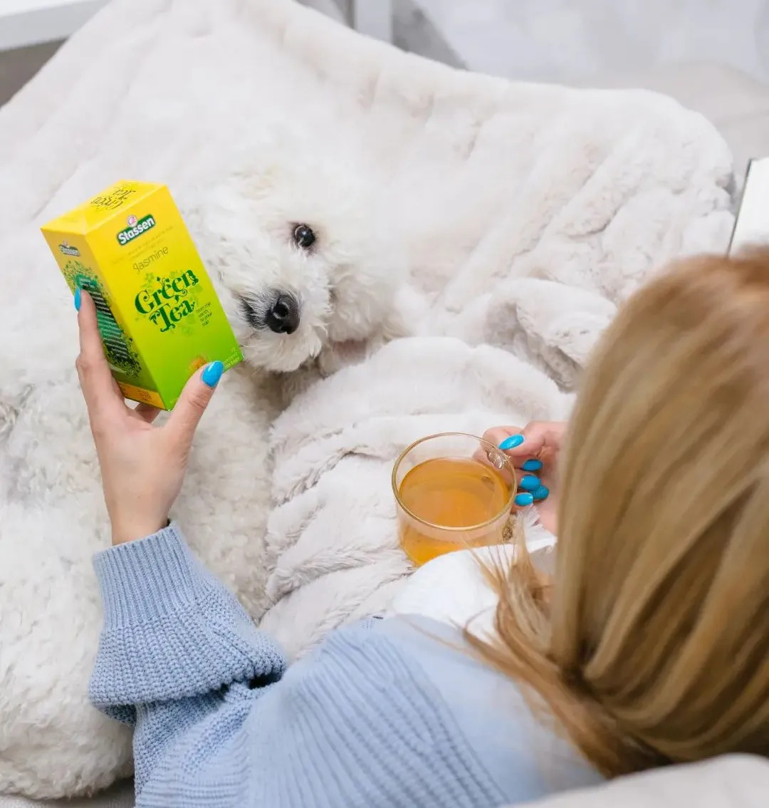 Person holding Stassen Jasmine Green Tea and a glass of brewed tea